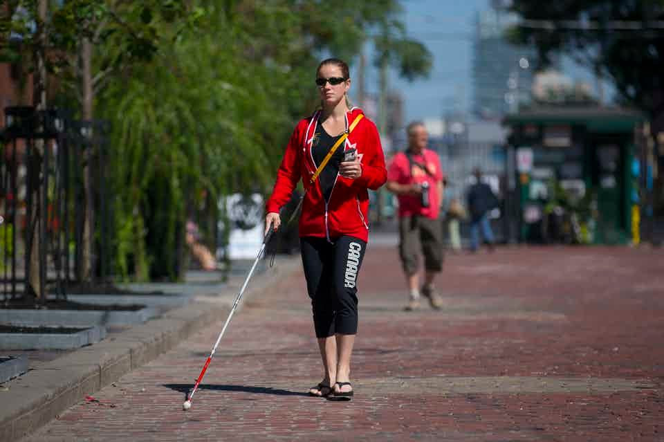 Blind woman using an assistive walking device while walking down a brick road.