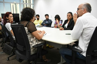 A imagem mostra várias pessoas sentadas em volta de uma mesa conversando.