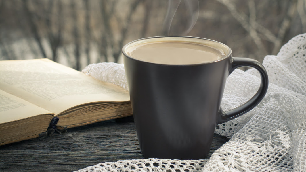Steaming mug of coffee on table with blanket and book