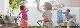 A woman and her children playing with hula hoops and a ball in their backyard.