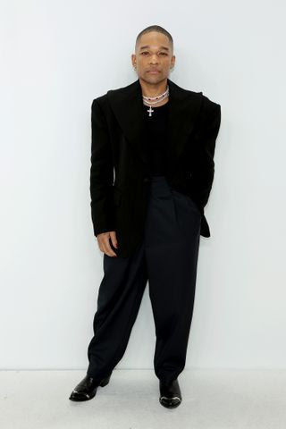 Image may contain Suit Clothing Formal Wear Coat Blazer Jacket Standing Person Adult Jewelry and Necklace