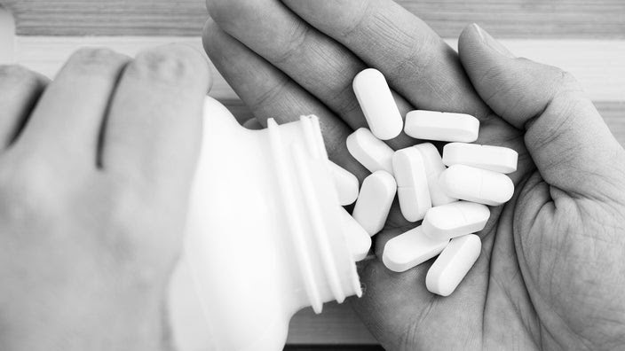 Black and white image of a person pouring magnesium supplements into their hand.