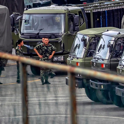 A members of People's Armed Police Force walk by vehicles at the Shenzhen Bay Sports Centre.  China has deployed paramilitary personnel, just across the border.
