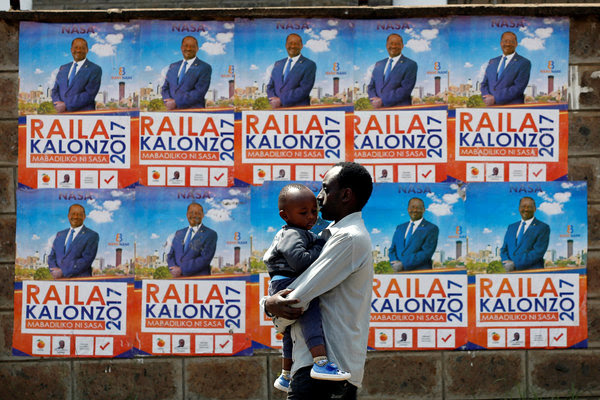 A man carries a child in front of campaign posters showing Kenyan opposition leader Raila Odinga on Aug. 6. (Baz Ratner/Reuters)</p>