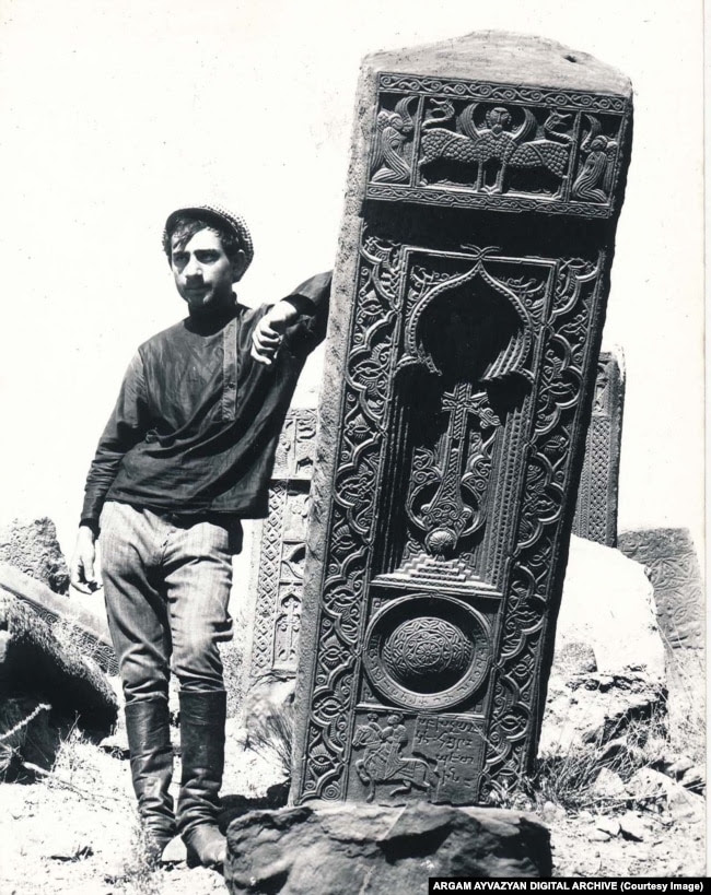 A man leans on a khachkar topped with a winged creature in the Julfa cemetery in 1915.