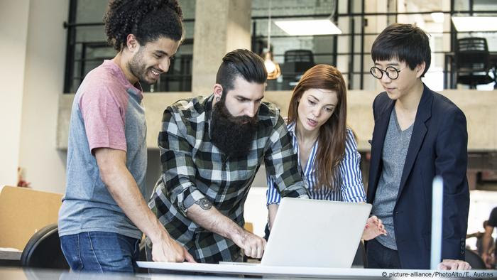 Jovens profissionais reunidos em volta de um notebook, usado por um deles para uma apresentação