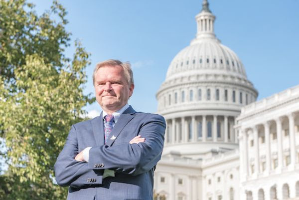 Scott MacConomy, Director of Policy ad Government Affairs at the Secular Coalition for America, wears a blue suit and stands with his arms crossed over his chest in front of the United States Capitol Building.