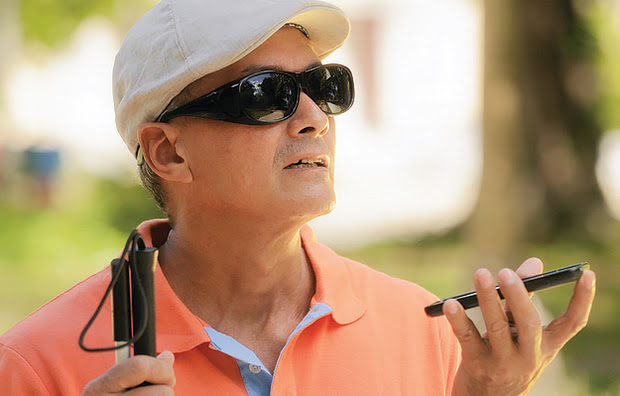 A vision impaired man holding a white stick and using a smartphone app.