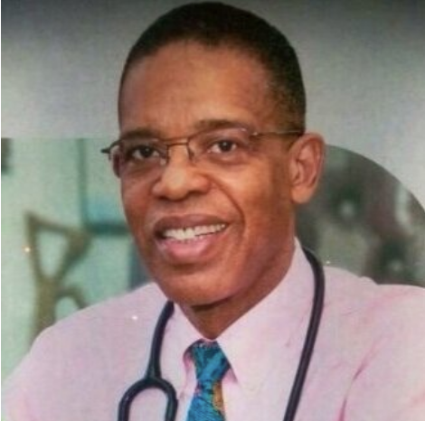 Headshot of a smiling bespectacled Black man wearing a pink

button-up shirt with a stethoscope around his neck.