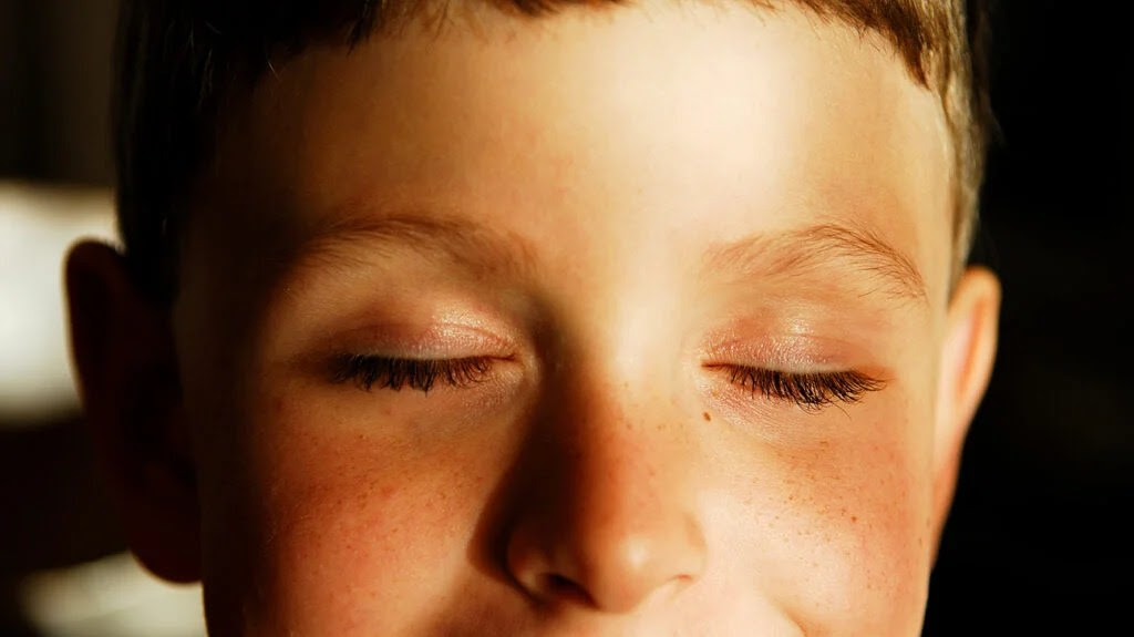 A child with their eyes closed and sun on his face