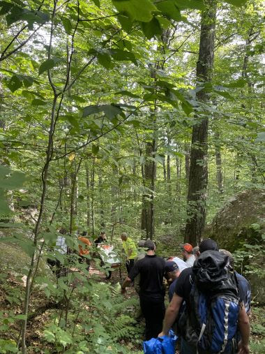 Rangers and EMS carrying injured hiker out of woods in a litter